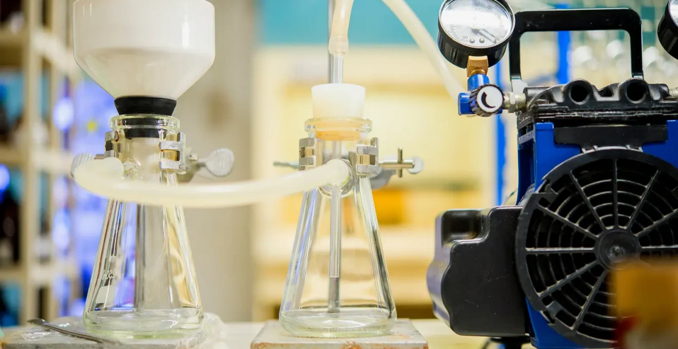 A scientist checks the pressure gauge of a benchtop membrane filtration unit connected to a peristaltic pump in a pilot hall.